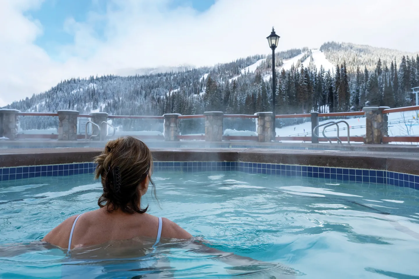 Person in a hot tub overlooking snowy mountains.
