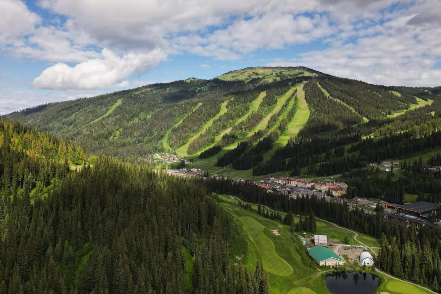 Sunny mountain landscape with vibrant green slopes and scattered clouds.