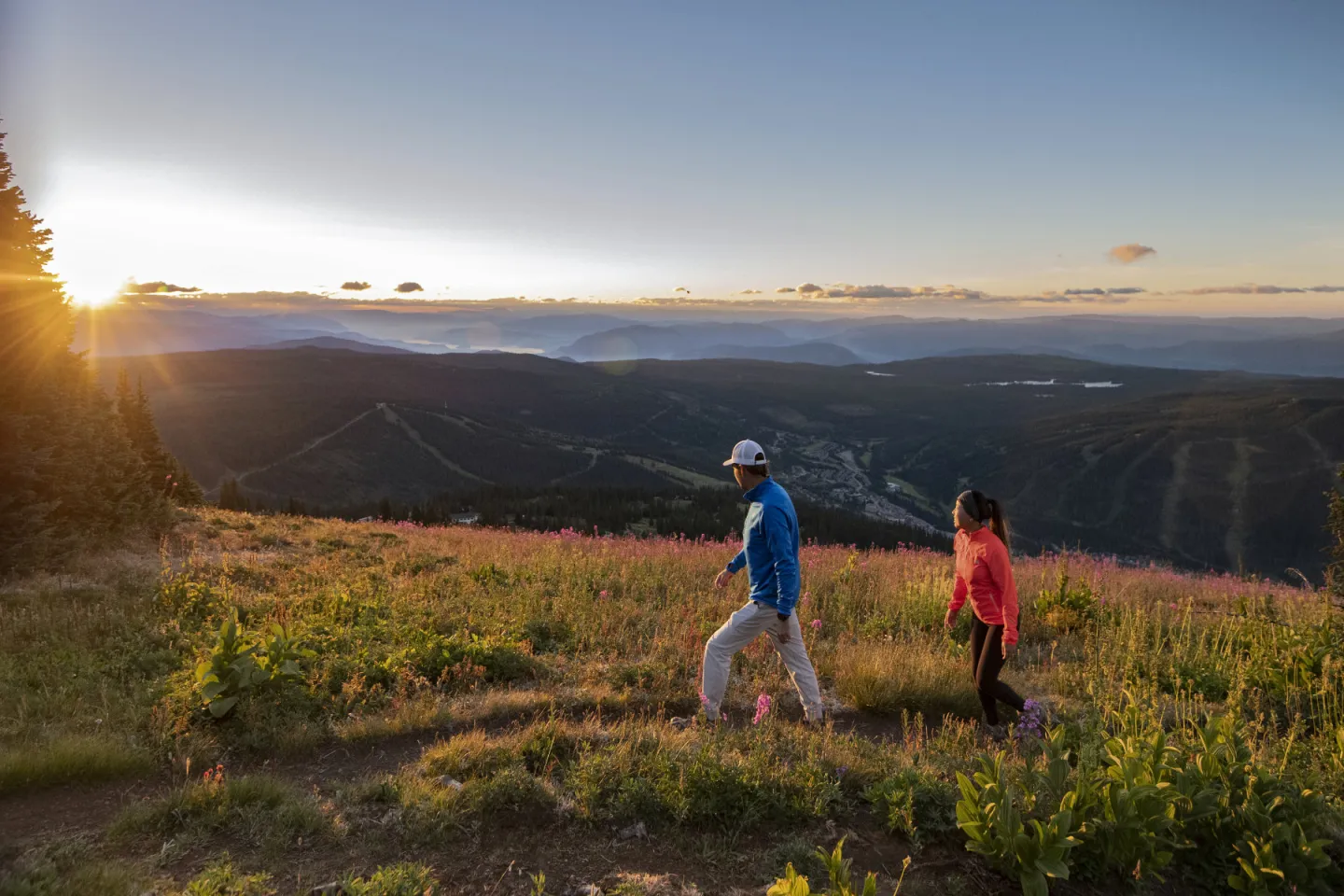 Two people hiking on a mountain trail at sunset, overlooking a valley.