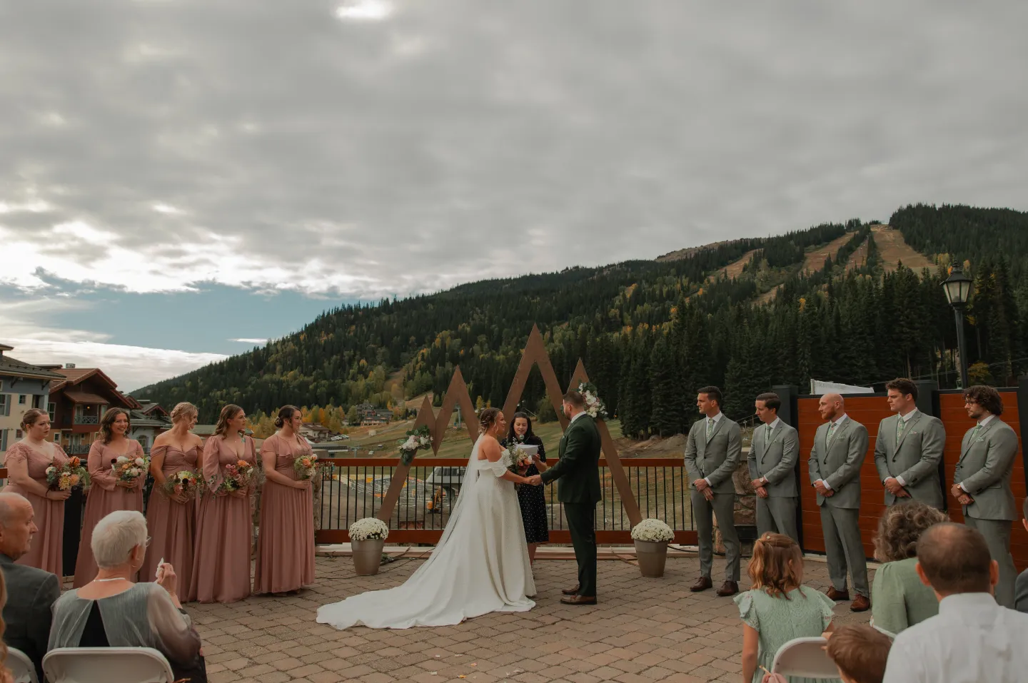 Outdoor wedding ceremony with mountains and a large bridal party.