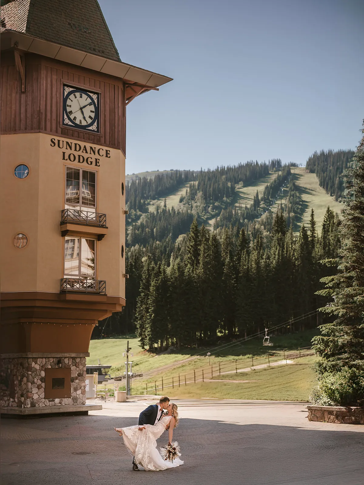 Bride and groom kiss outside a lodge, mountain backdrop.