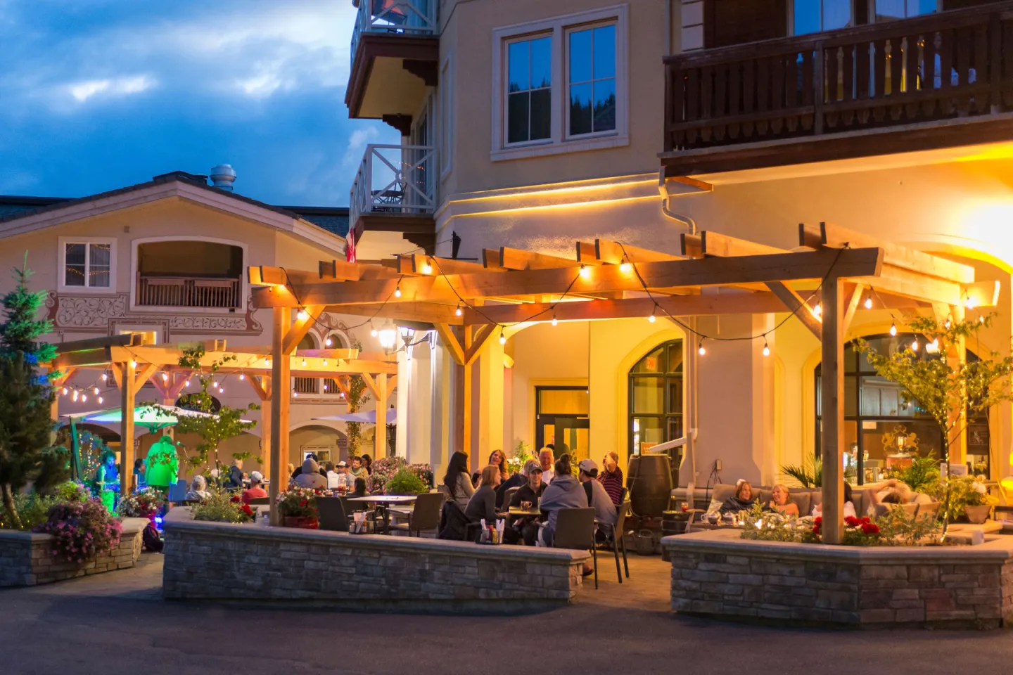Outdoor restaurant patio at dusk with warm lighting and patrons dining.