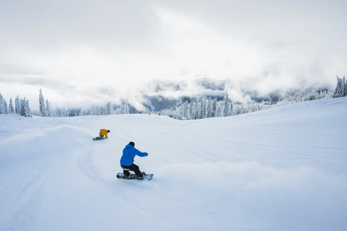 Two snowboarders carving through a snowy mountain slope.