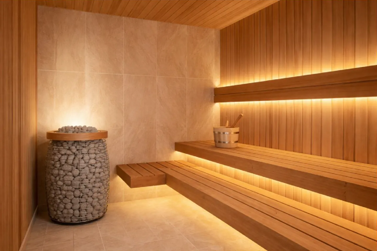 Warm wooden sauna interior with tiered benches, soft lighting, and a stone heater.
