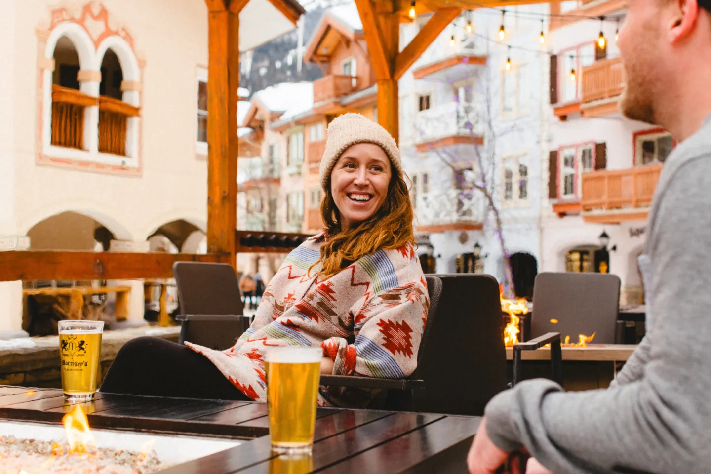 Woman laughing with a man at an outdoor patio, beers on the table.