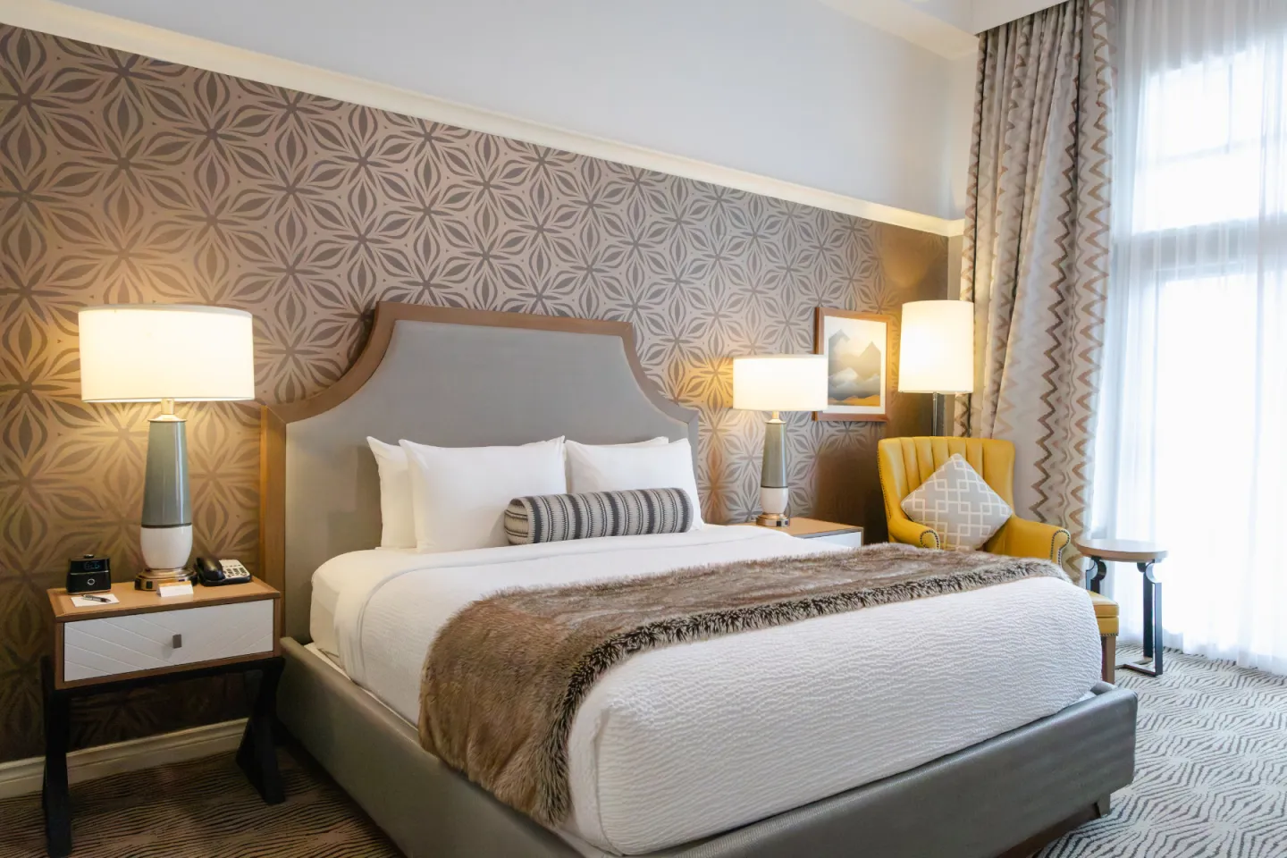 Elegant hotel bedroom with a large bed, patterned wallpaper, and bedside lamps