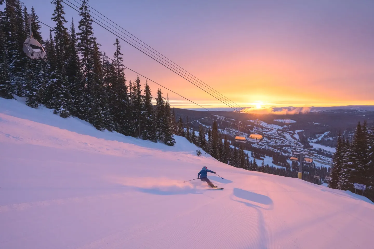 Skier carving through snow at sunset above a mountain town.